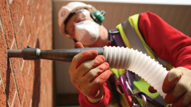a worker attaches a tube to a brick wall to inject insulation