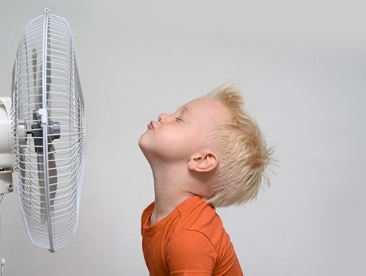 Boy cooling his face with an electric fan