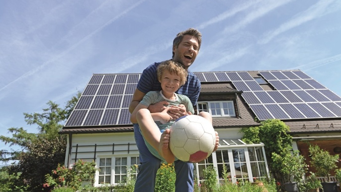 Solar panels on roof of detached family home with father and son playing football in front