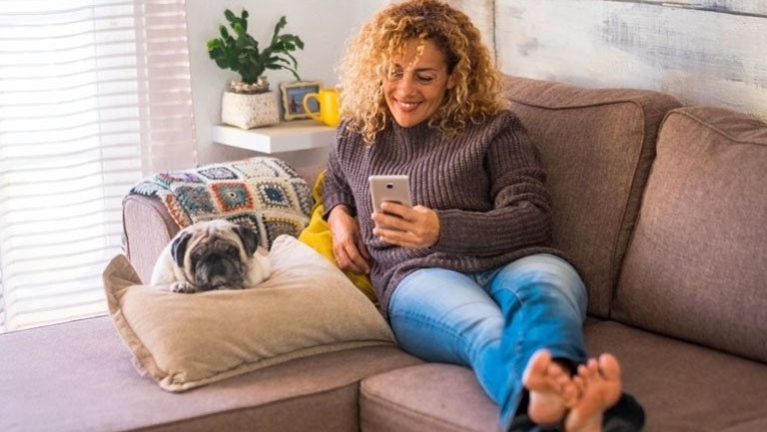 Woman scrolling on phone whilst on sofa, 50% off BoilerCare promo ribbon in corner